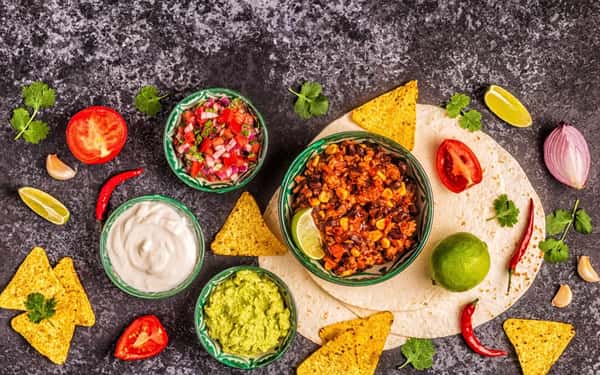 Mexican appetizer spread with tortilla chips, guacamole, sour cream, pico de gallo, and chili with corn in festive bowls.