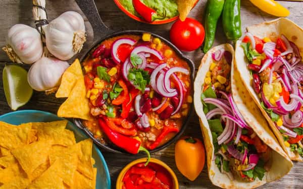 Tacos and skillet chili with beans, corn, red onions, and peppers, served with tortilla chips, lime, and guacamole.