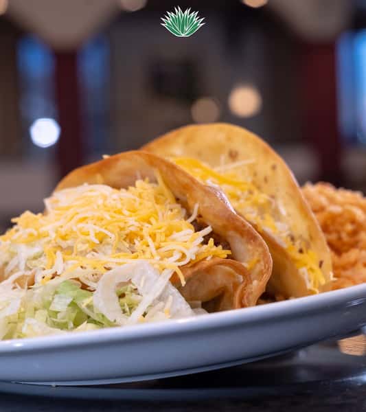 Crispy beef tacos topped with lettuce and shredded cheese, served with Mexican rice and refried beans