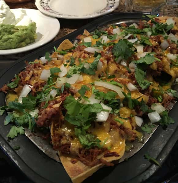 Loaded nachos topped with meat, cheese, cilantro, onions, and jalapeños