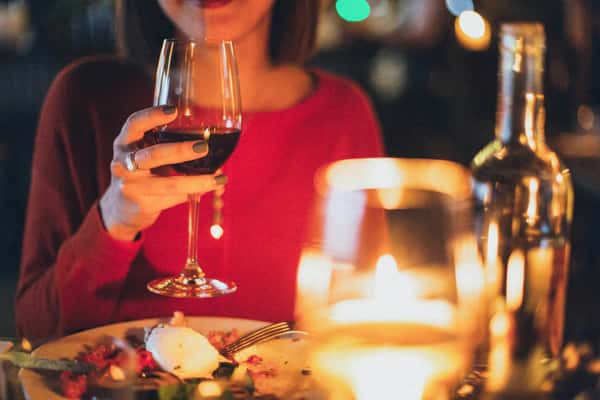 Woman in a red sweater holds a glass of red wine at a candlelit table in City Limits Bar and Grill.