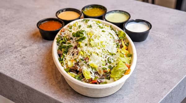 Burrito bowl with beef, lettuce, cheese, and cilantro, served with four sauces in black cups.