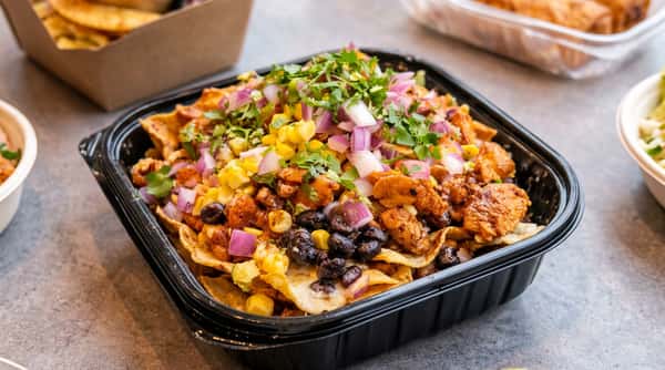 Nachos topped with chicken, black beans, corn, red onion, and cilantro in a black container.