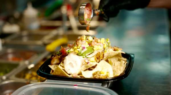 Nachos with chicken, corn, avocado, red onion, and salsa being spooned on top.