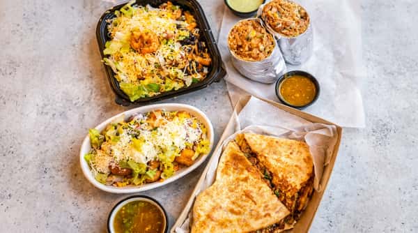 Assortment of Mexican dishes: a shrimp rice bowl, two foil-wrapped burritos, tater tot bowl, and cheese quesadilla.