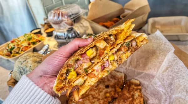 Hand holding a quesadilla slice with melted cheese, chicken, corn, and red onion.