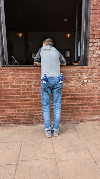 man looking into the window with bottled drinks in his back pockets