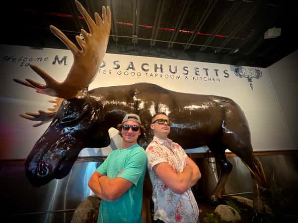 two guys standing back to back in front of a moose statue