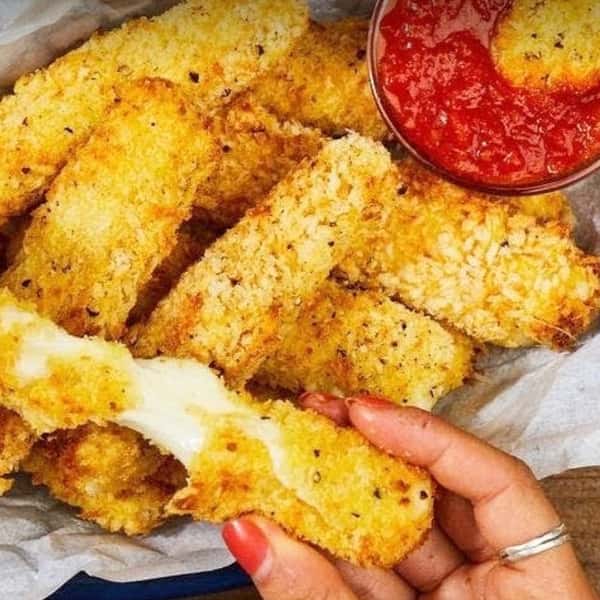 Crispy breaded mozzarella sticks served hot with marinara dipping sauce, featuring golden fried cheese pulls in a casual Italian restaurant appetizer setting.