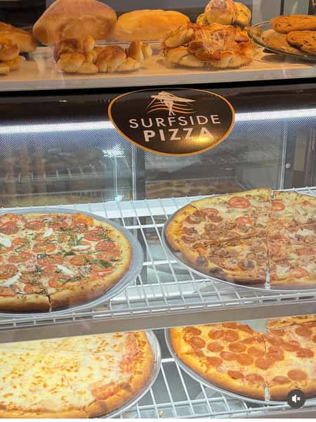 Assorted specialty pizzas on display at Sureside Pizza, including pepperoni, cheese, and veggie options in a glass case, highlighting a local Italian pizzeria with fresh baked goods and a welcoming atmosphere.