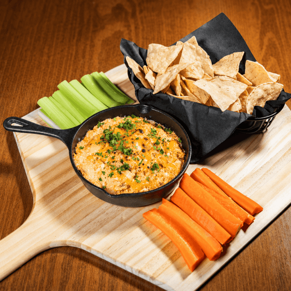 Cheese dip in a cast iron skillet with tortilla chips, celery, and carrot sticks