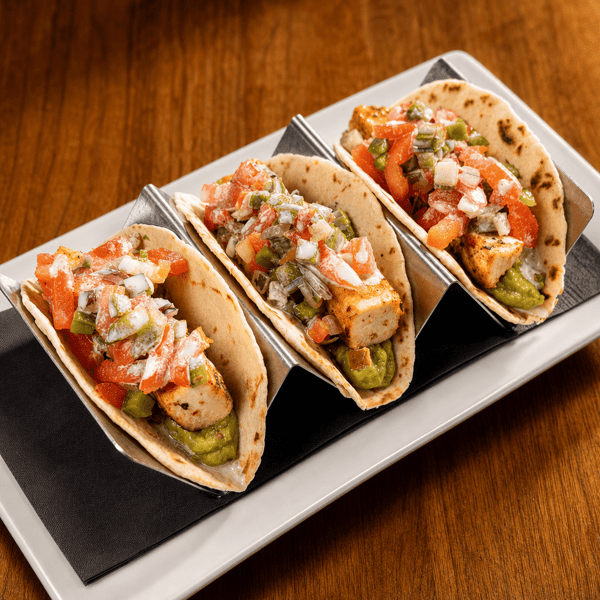 Three fish tacos topped with pico de gallo, served on a black tray