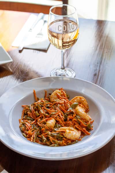 Shrimp pasta in a white bowl with a glass of white wine