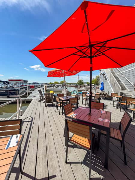 Outdoor patio seating with a red umbrella overlooking the marina