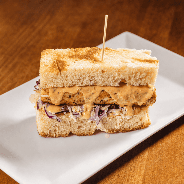 Sandwich with grilled meat, red cabbage slaw, and sauce, secured with a skewer