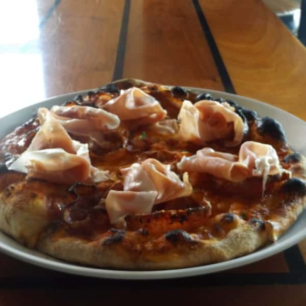 Wood-fired pizza topped with prosciutto and tomato sauce
