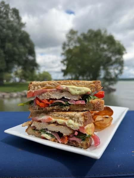Stacked sandwich sliced in half and served with chips, overlooking the water