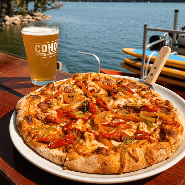 Pizza topped with peppers and vegetables served with a glass of beer by the lake