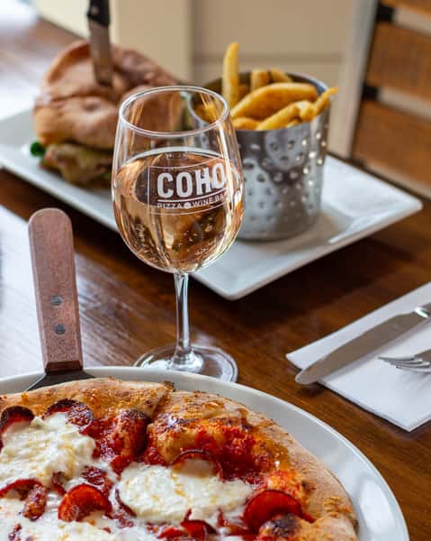 Table setting with pizza, a sandwich, fries, and a glass of rosé wine
