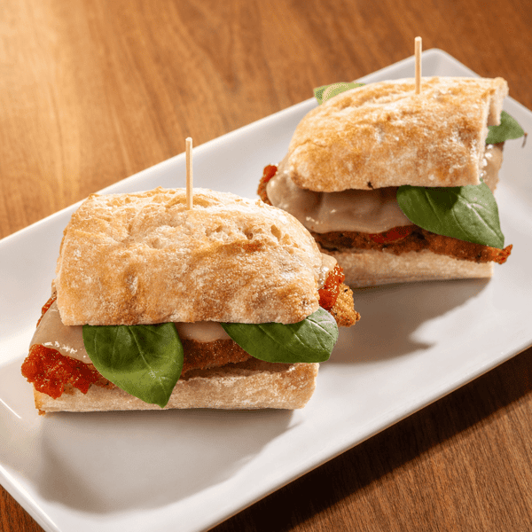 Two mini sandwiches with prosciutto and basil on ciabatta bread