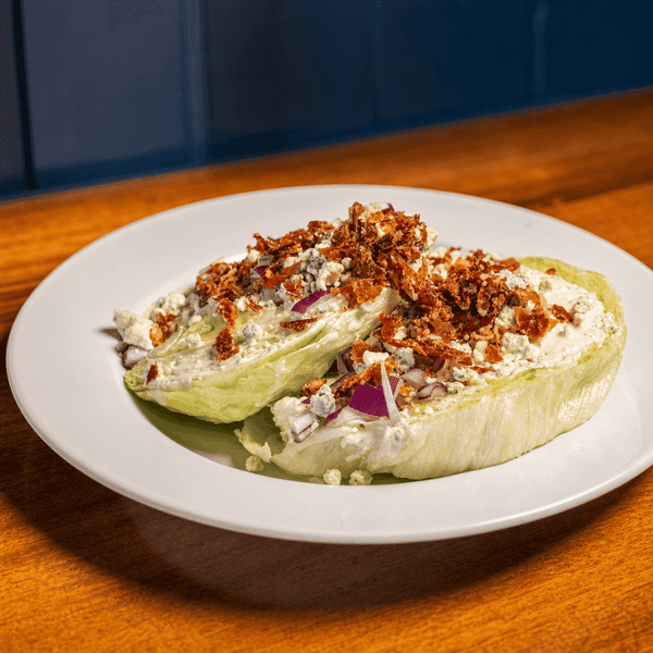 Overhead view of a wedge salad with blue cheese dressing, bacon bits, and red onion