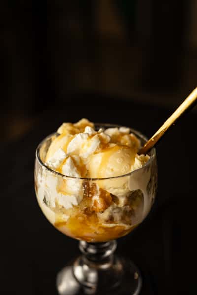 customized sundae with caramel, pecans, and whipped cream sitting on top of vanilla ice cream in a glass.