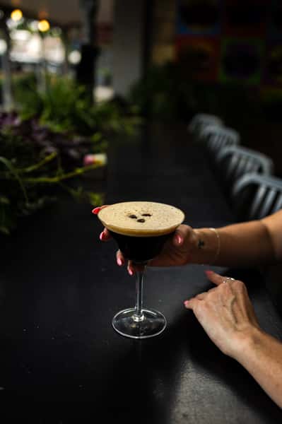 our classic espresso martini is being held by a customer, with a black bar and plants in the background.
