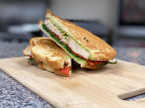 Boulevard Cafe's chicken pesto panini with roasted red peppers and greens on a wooden board.