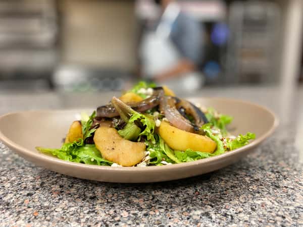 Boulevard Cafe's vibrant salad features crisp greens, roasted pears and onions, and crumbled cheese in a modern beige bowl.
