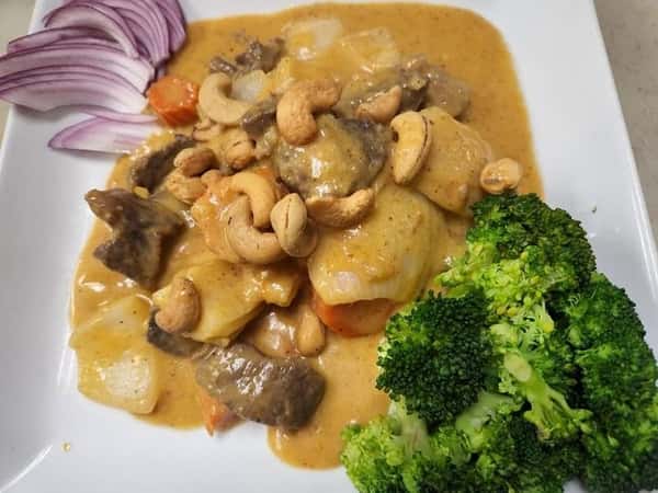 Thai cashew nut stir-fry with beef, onions, bell peppers, and carrots in a savory brown sauce, topped with roasted cashews and served with a side of steamed broccoli and red onions.