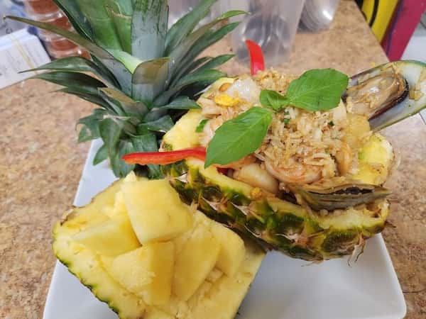 Pineapple fried rice with shrimp, mussels, and vegetables served in a halved pineapple shell, garnished with fresh basil and red chili—tropical Thai seafood dish with a stunning presentation.