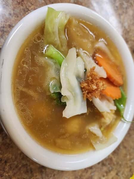 Bowl of Thai vegetable soup with cabbage, carrots, broccoli, and garlic in a clear savory broth—comforting and healthy soup perfect as a starter or side dish.