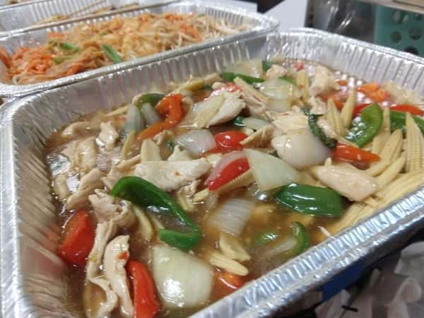 Colorful chicken stir-fry with bell peppers, onions, baby corn, and snap peas in a glossy sauce, served in a catering tray, ideal for buffet-style dining.