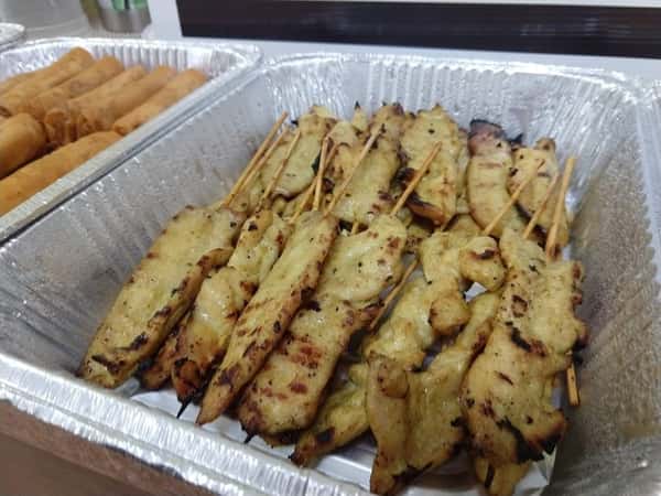 Grilled chicken satay skewers served in a foil tray, featuring tender marinated slices with light charring, ideal for Thai or Southeast Asian cuisine menus.