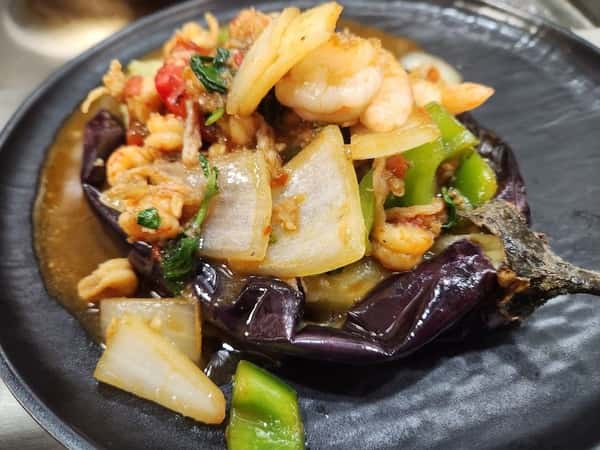 Stuffed eggplant topped with sautéed shrimp, onions, green peppers, and Thai basil in a savory garlic sauce, served on a black plate—perfect for a spicy seafood and vegetable fusion dish.
