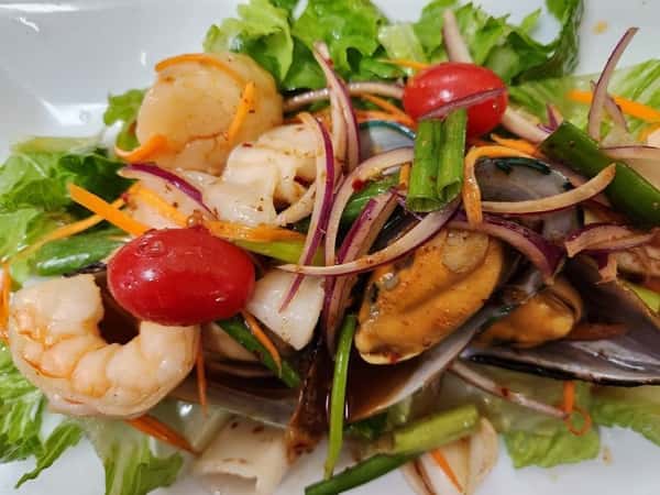 Spicy Thai seafood salad with shrimp, mussels, squid, red onions, cherry tomatoes, and mixed greens tossed in a tangy chili-lime dressing, perfect for Thai cuisine lovers.