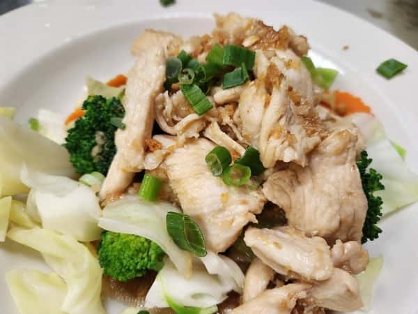 Sautéed chicken breast strips over stir-fried vegetables including broccoli, cabbage, and carrots, garnished with chopped green onions on a white plate.