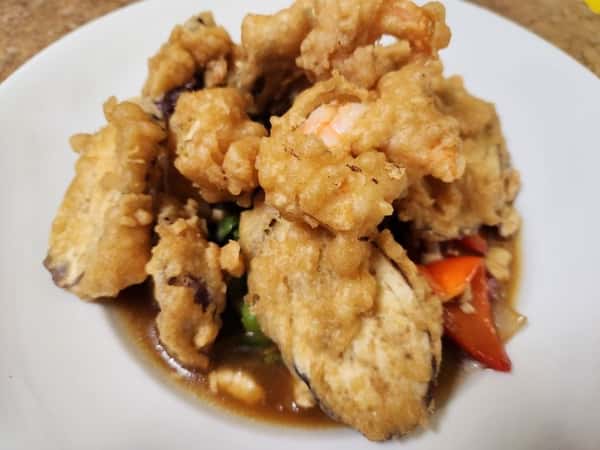 Deep-fried tempura shrimp and vegetables in a savory brown sauce, served in a white bowl, featuring a crunchy and flavorful Asian-style entrée.