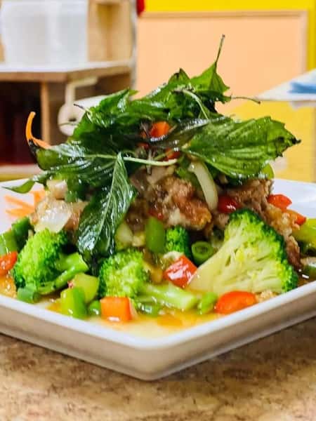 Crispy chicken topped with Thai basil leaves and served over sautéed vegetables including broccoli, bell peppers, and onions in a flavorful brown sauce.