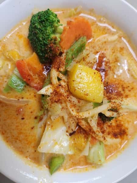 Thai red curry with mixed vegetables including broccoli, carrots, cabbage, and bell peppers in a creamy coconut base, garnished with chili powder for an extra kick.