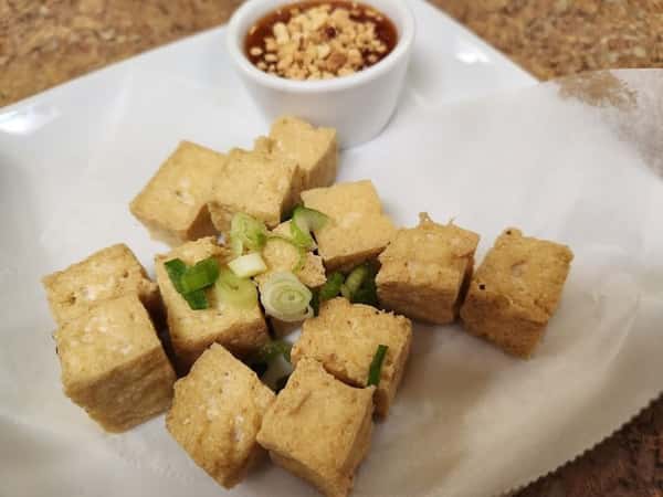 Golden crispy tofu cubes garnished with chopped green onions, served with a side of tangy peanut dipping sauce—classic vegan appetizer with a crunchy texture and nutty flavor.