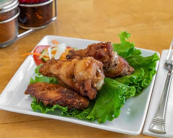 Thai-style crispy fried chicken wings served on a bed of fresh lettuce with a side of sliced tomato and shredded vegetables—perfect as a savory appetizer or shared starter.