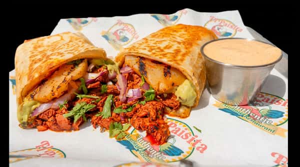 Two large burritos, one cut in half, filled with meat, red onion, and cilantro, served with a side of sauce on branded paper.
