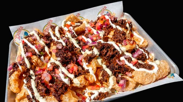 Chicharrones with shredded meat, diced tomatoes, red onions, and white crema on a metal tray.