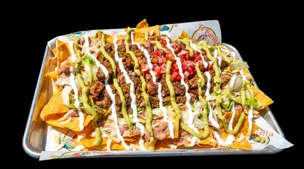 Nachos in a tray, topped with meat, beans, guacamole, sour cream, pico de gallo, and shredded lettuce.