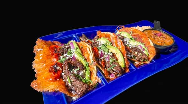 Three tacos with steak, avocado, and red onion on a blue plate, with a side of beans.