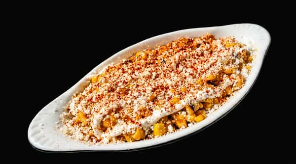 Elote corn salad in a white dish, topped with white cheese and red spices.