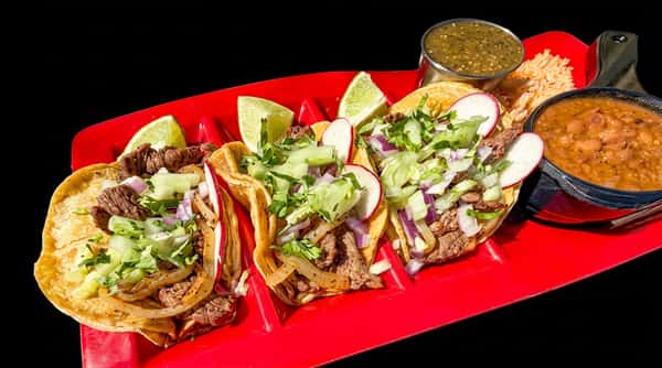 Three carnitas tacos with cilantro, onions, and limes, served with rice, refried beans, and salsa in a red dish.