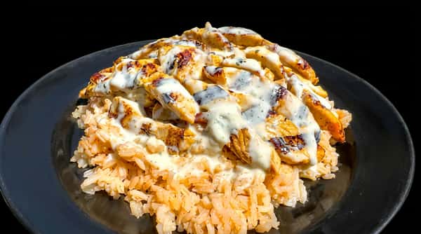 Grilled chicken strips with white sauce over orange rice on a black plate.