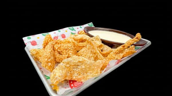Crispy chicharrónes with a side of creamy dip, served on a paper-lined tray.